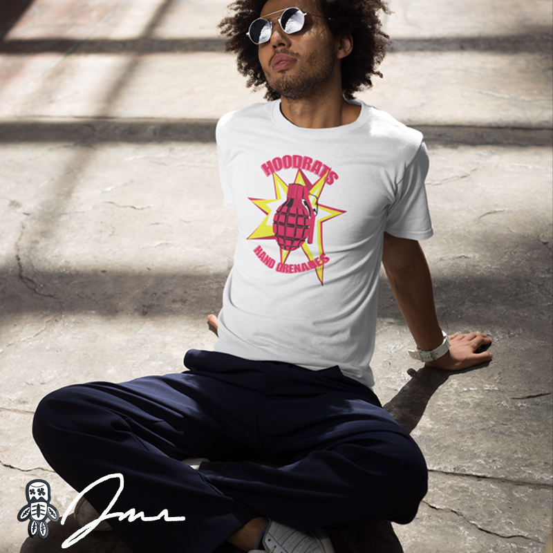 a man modeling a white tshirt that has a yellow and red pineapple grenade exploding the words hoodrats & hand grenades as he is leaning back on the ground with sunglasses on looking up at the sky